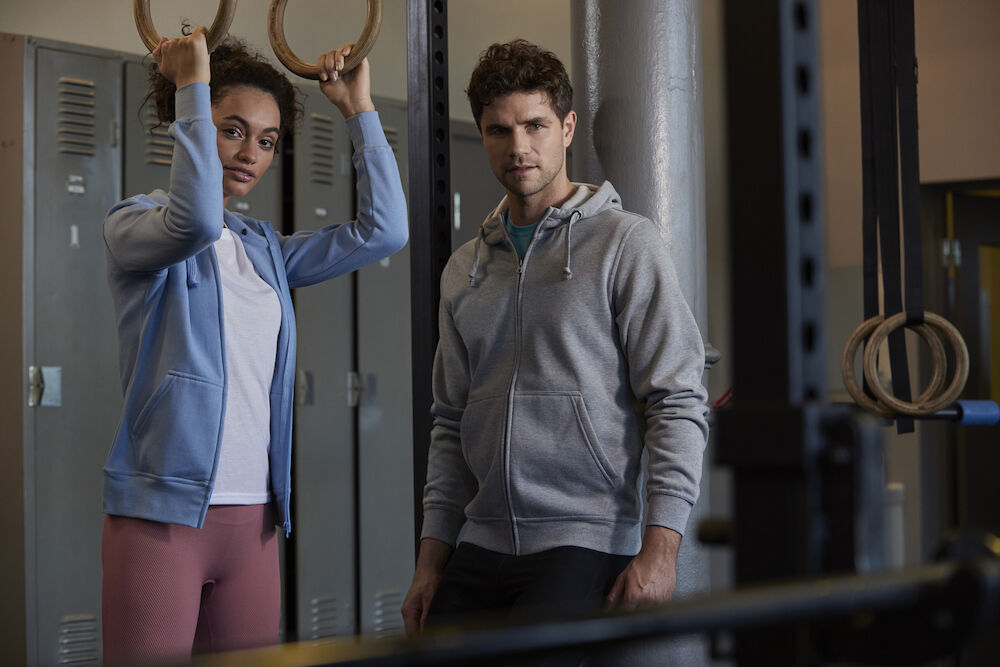 Felpe palestra Un uomo e una donna in piedi davanti a una palestra. Abbigliamento personalizzato per abiti da lavoro con stampa di alta qualità.